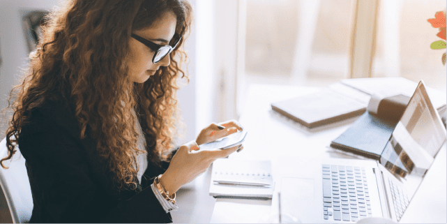 Woman at computer at workplace on her phone with social media.