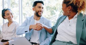 Three people sitting down and meeting each other, two are shaking hands.